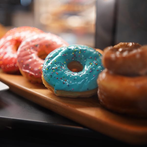 A row of colorful, frosted donuts with sprinkles on a wooden board at Karma Kolache & Dessert.