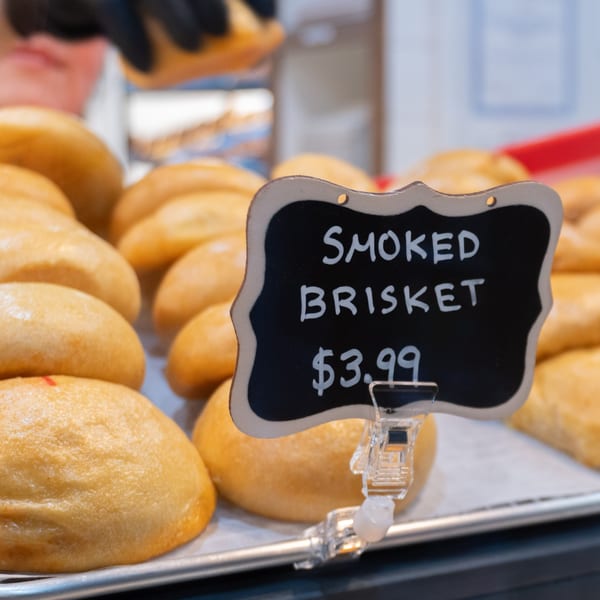 Tray of golden-brown smoked brisket kolaches with a chalkboard sign displaying the price.