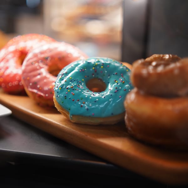 A row of colorful, frosted donuts with sprinkles on a wooden board at Karma Kolache & Dessert.